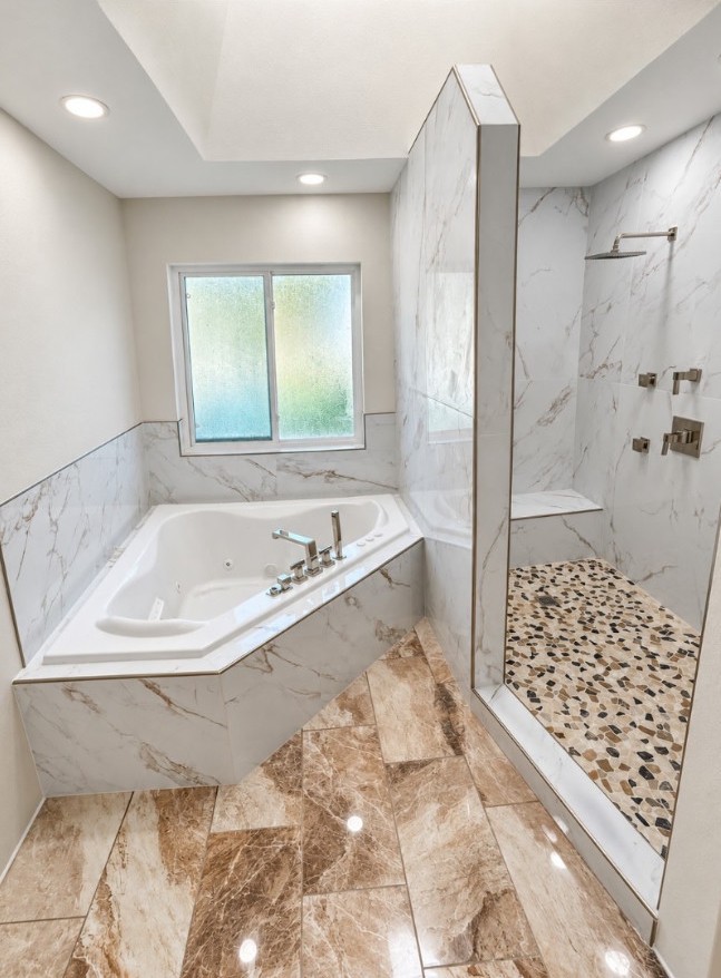 Bright bathroom with a tub, marble-patterned tiled shower walls, pebble shower floor and polished floor tiles.