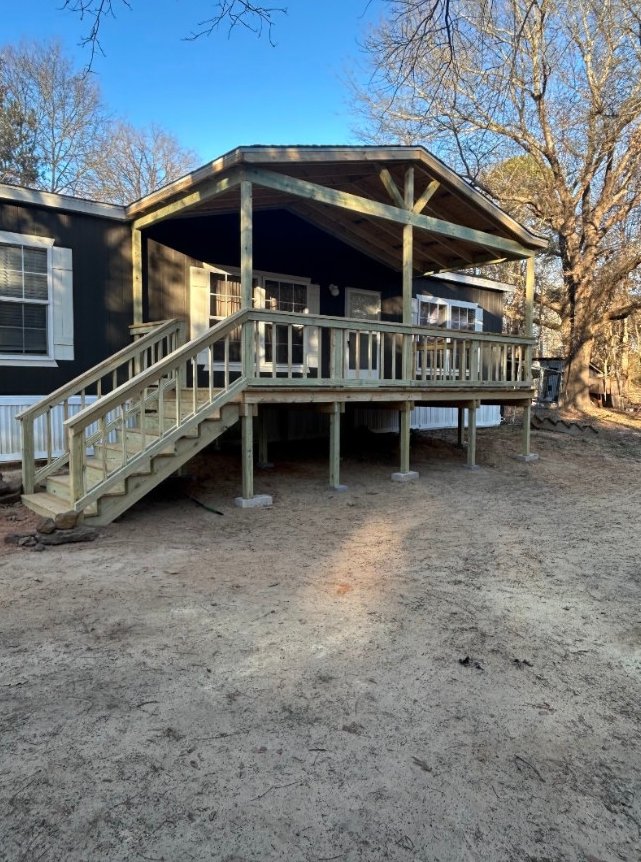 Elevated covered wood porch with exposed posts, railings and stairs at the left.