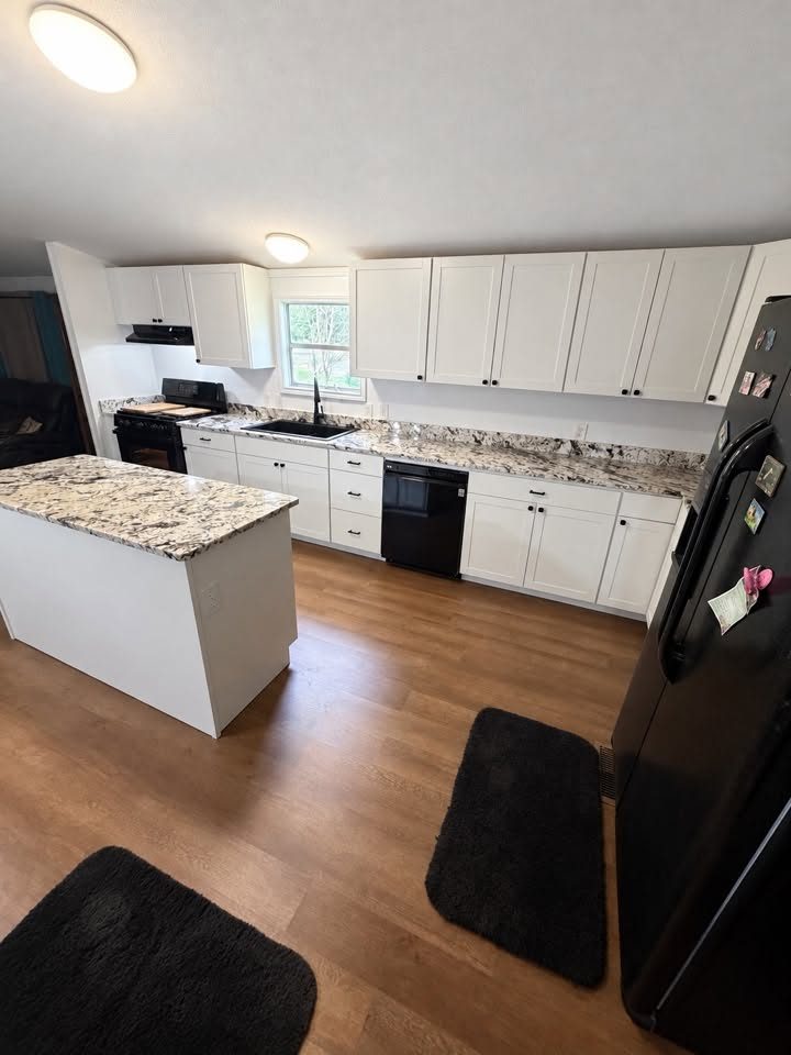 Kitchen with white cabinets, island, patterned counters and wood-look flooring.